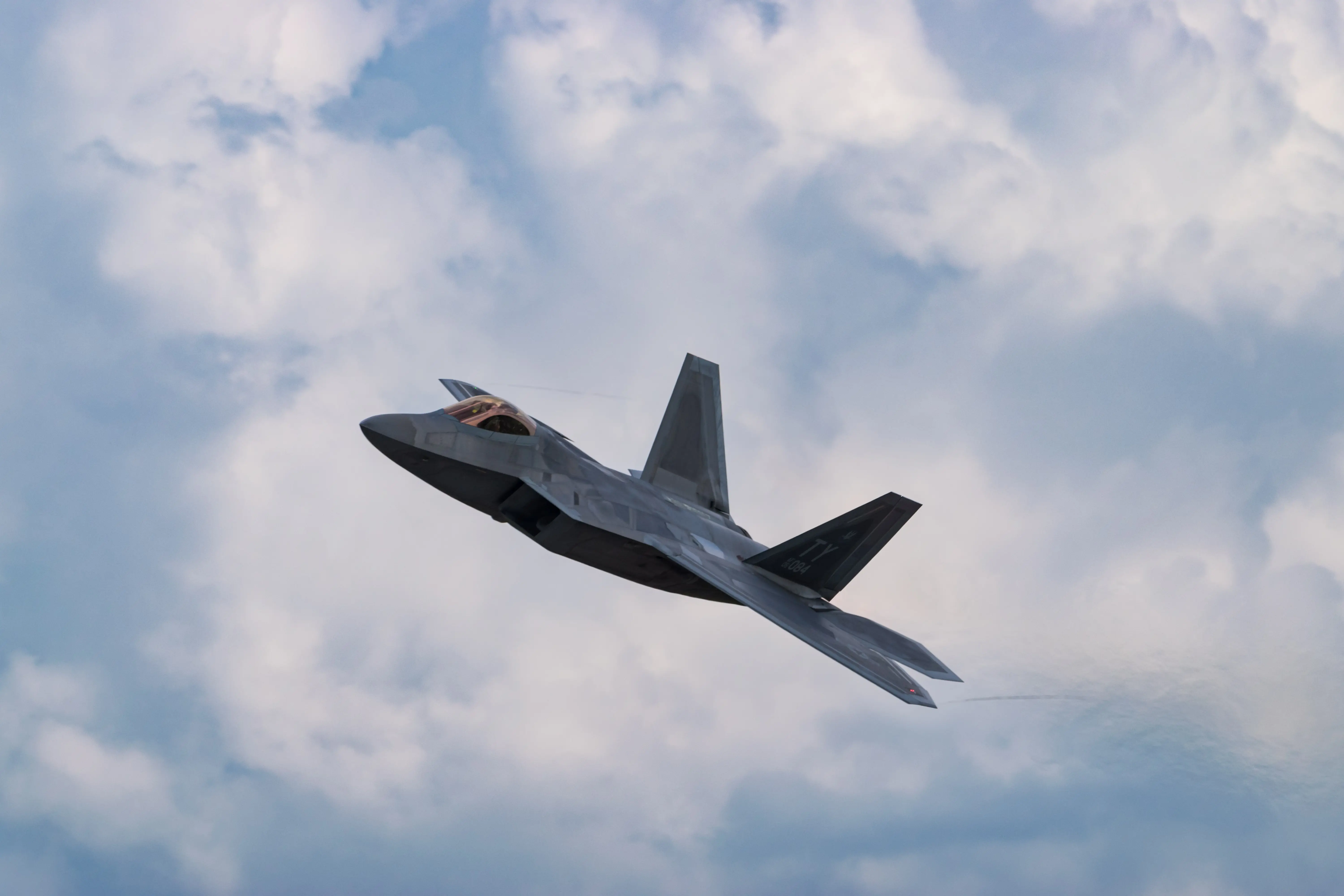 F-22 aircraft banking above the clouds
